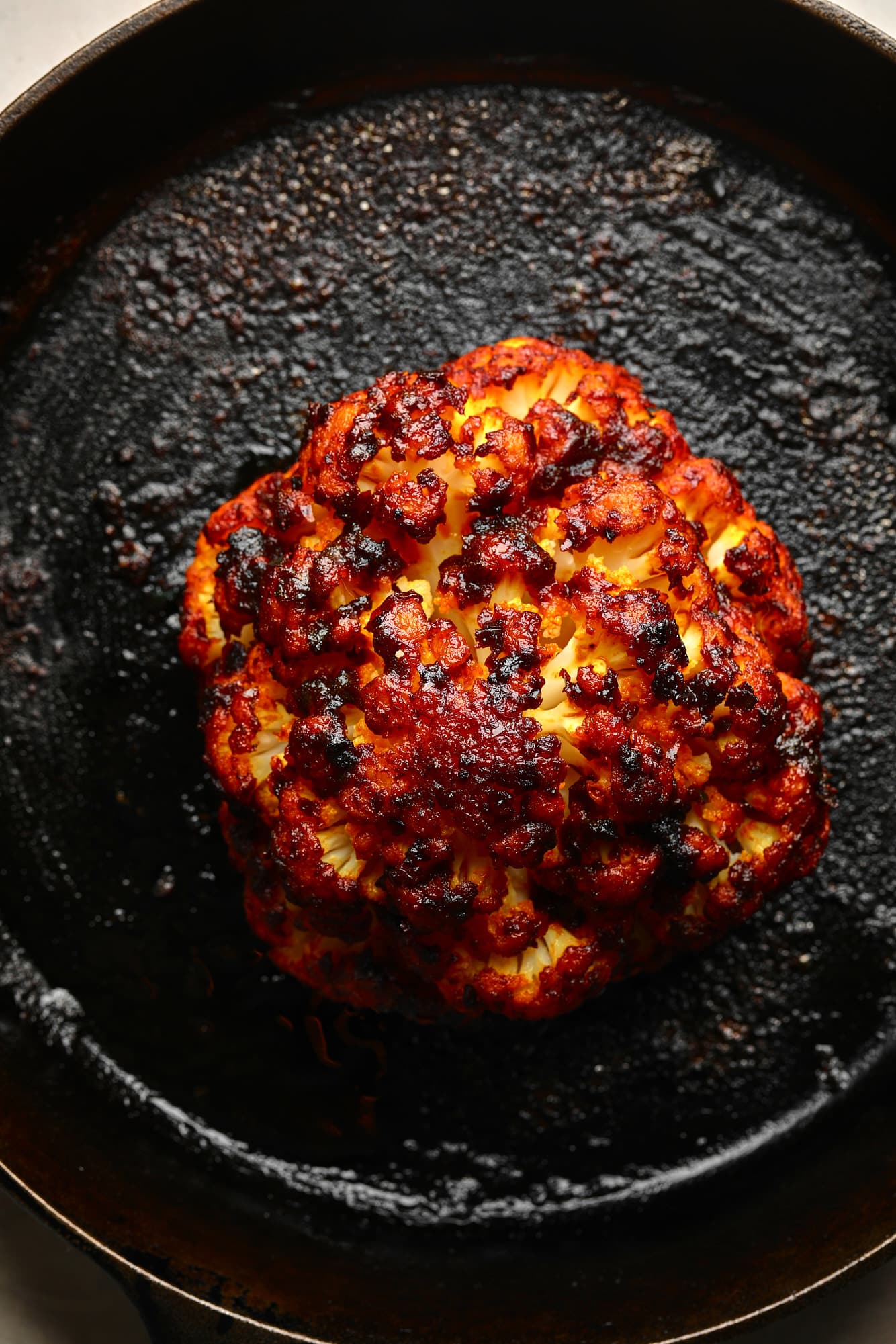 Uma cabeça de couve-flor assada com vias de Harissa em uma frigideira preta.