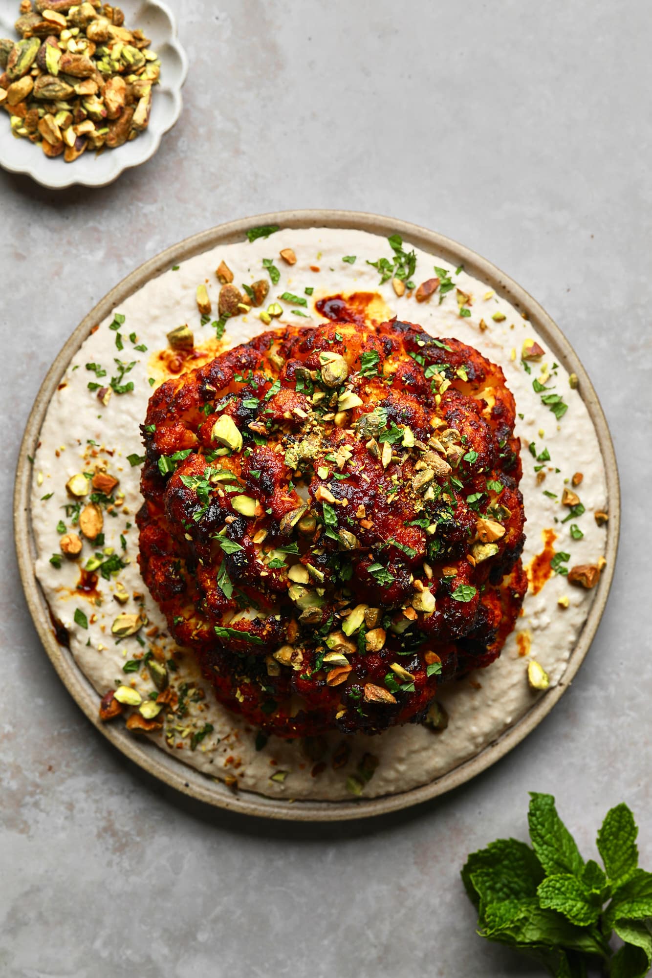 Uma cabeça de couve-flor assada com brilho harissa em um feijão branco espalhado em um prato.