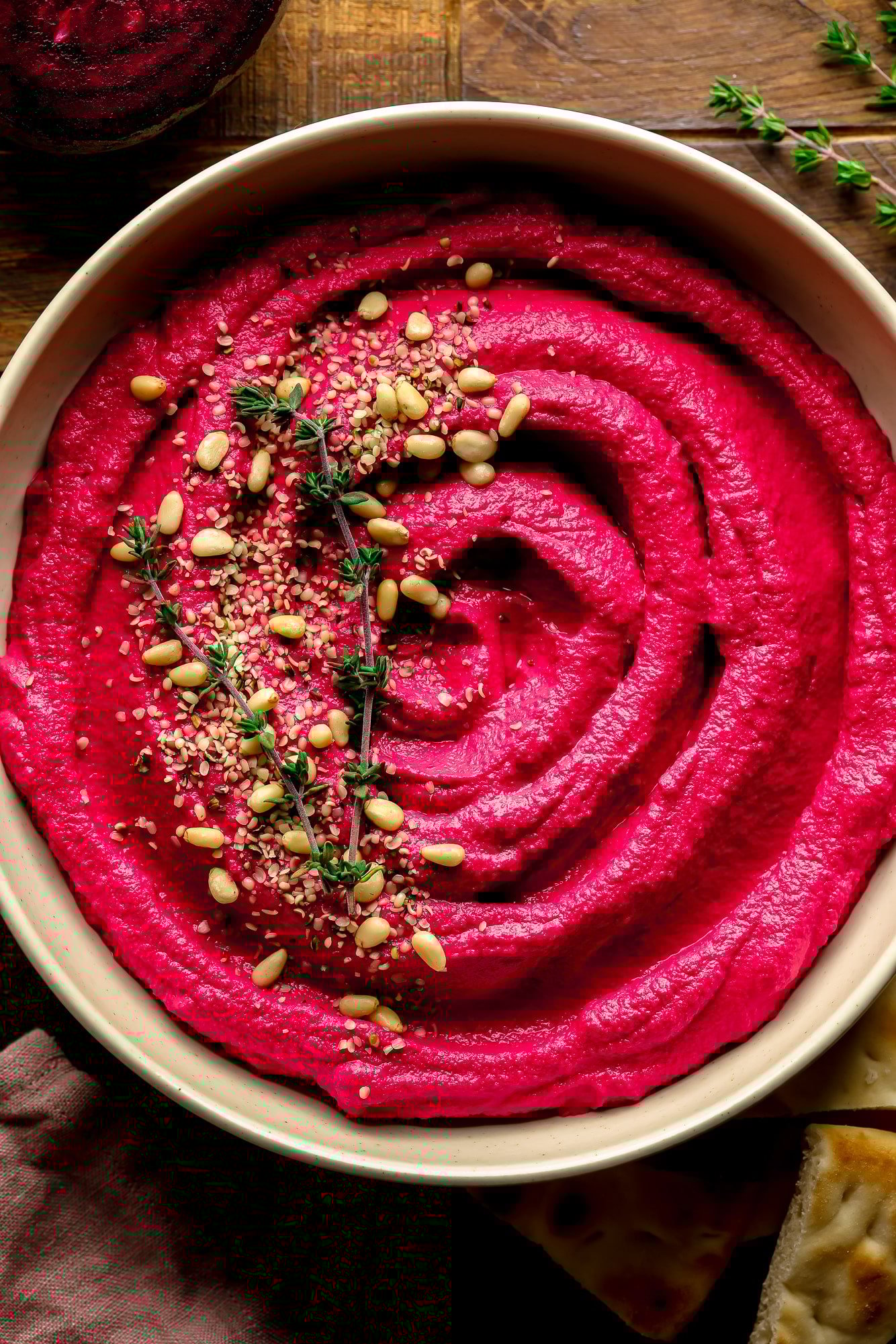 Uma tigela de hummus rosa com pinhões e tomilho por cima.