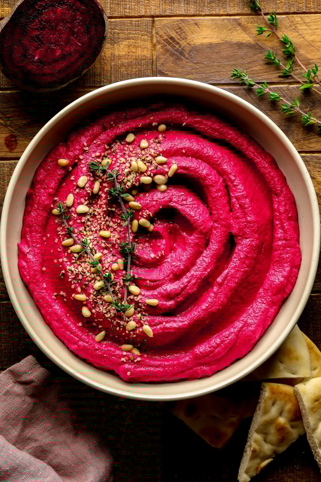 Uma tigela de hummus rosa com pinhões e tomilho por cima.