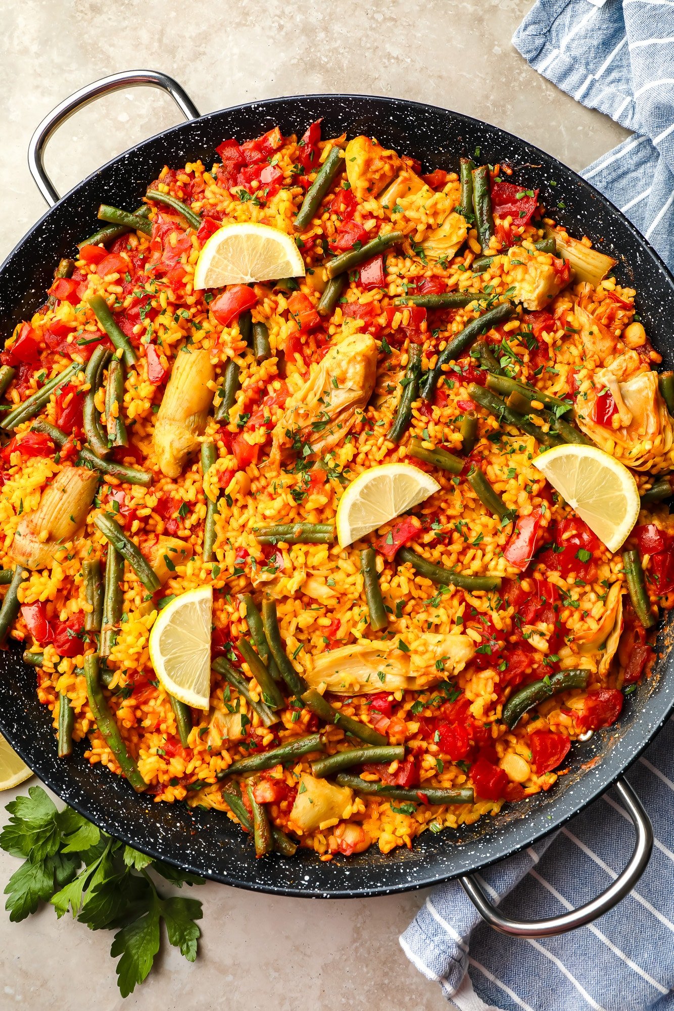 Paella vegana coberta com fatias de limão em uma grande paella preta.