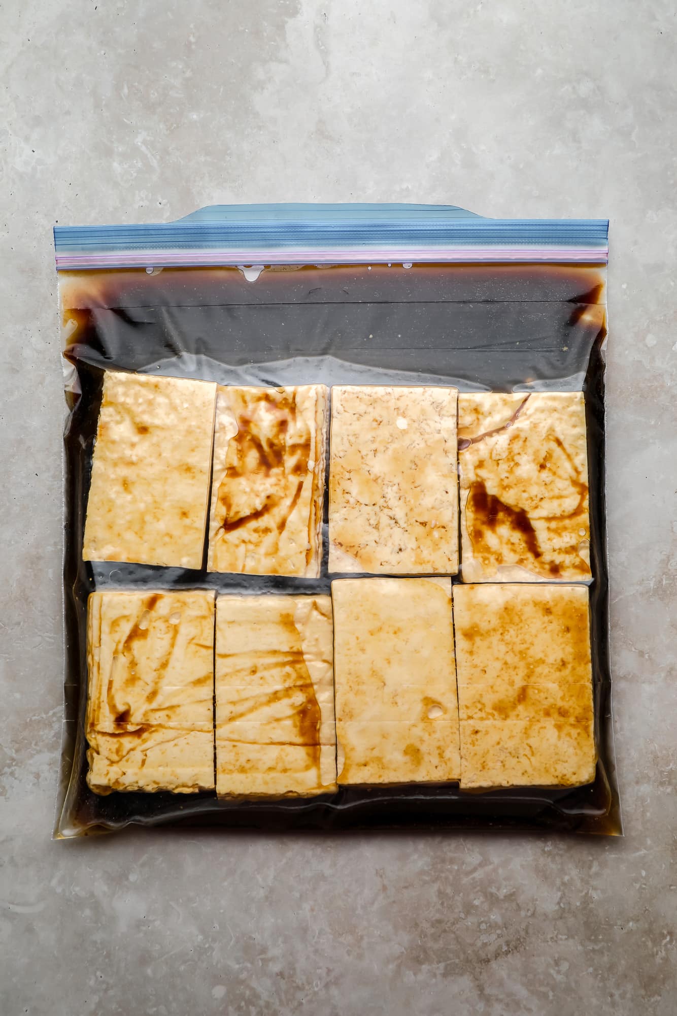 Pedaços retangulares de tofu e uma marinada em uma grande bolsa de ziplock.