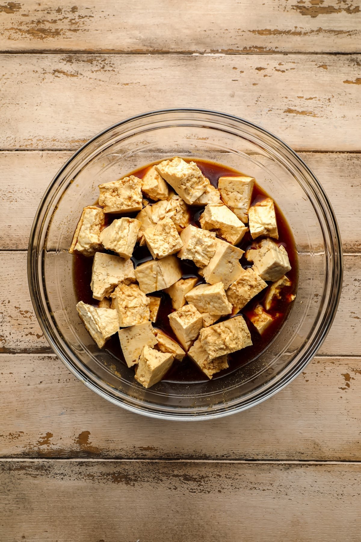 Pedaços de tofu rasgados em uma tigela de vidro com molho de soja marinada em fundo de madeira