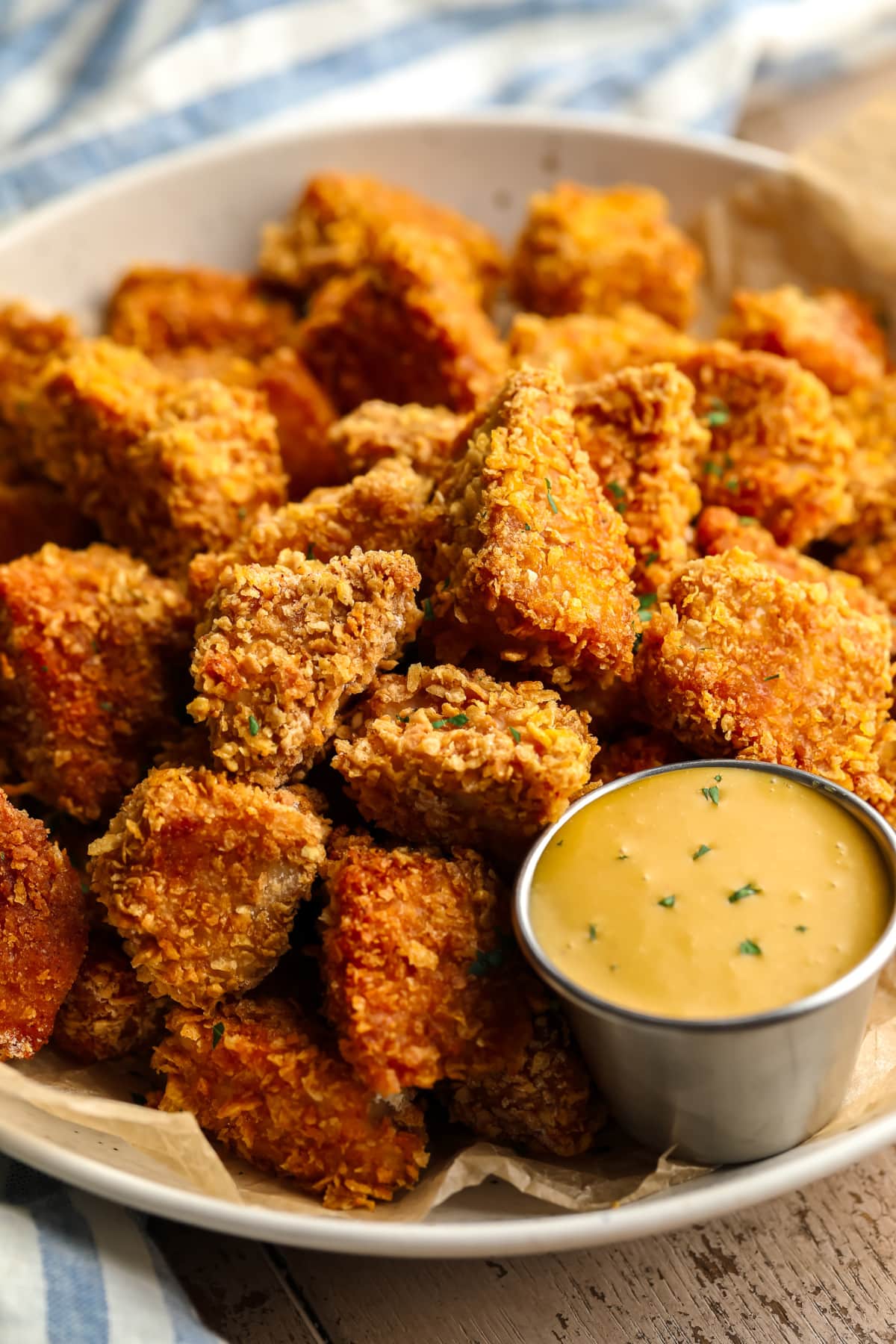 Nuggets de frango vegano à milanesa crocante em uma tigela rasa com molho amarelo, toalha azul em fundo